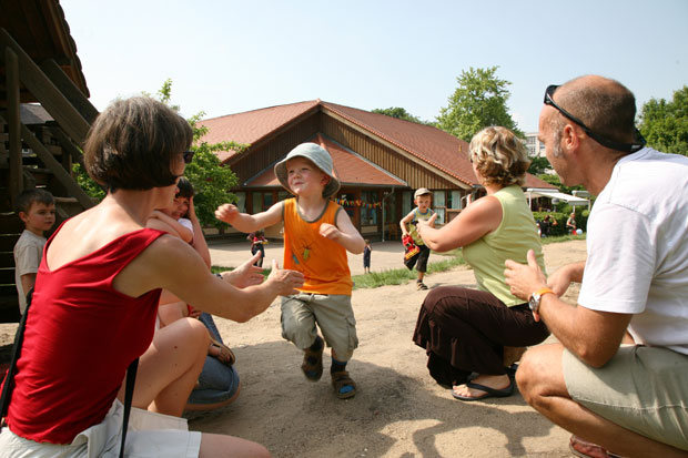 Ein Sandkasten auf einem Spielplatz. Zwei Kinder laufen lachend ihren wartenden Eltern entgegen