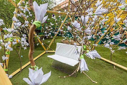 Sitzbank aus Metall mit weißen Polstern, darum an Zweigen gebastelte weiße Magnolienblüten