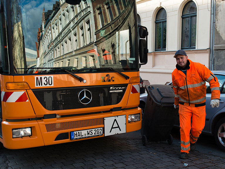 oranges Fahrzeug zur Entleerung der Abfalltonnen und ein Arbeiter in oranger Kleidung
