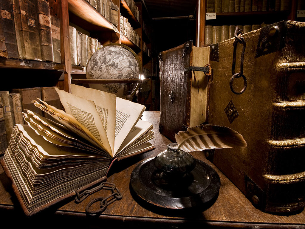 Alte Gegenstände - ein aufgeschlagenes Buch, Tintenfass mit Federkiel, Globus - in einem Raum mit spärlichem Licht